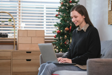 Happy young woman using laptop on sofa enjoying online shopping during winter holiday season..の写真素材