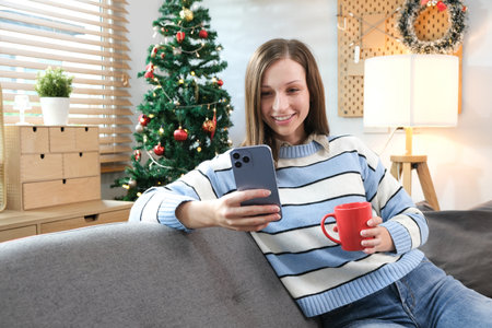 Beautiful woman with phone drinking tea at home on Christmas eve.の写真素材
