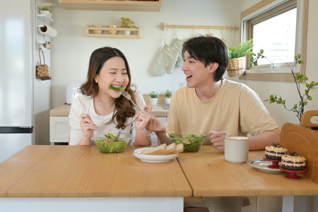 A man and woman are eating together at a table. They are both smiling and seem to be enjoying their meal..の写真素材