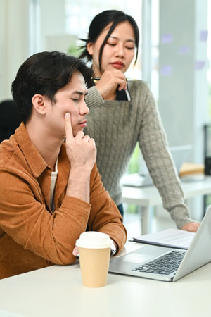 A man and a woman are sitting at a table with a laptop and a cup of coffee. The man is looking at the laptop while the woman is looking at him.の写真素材
