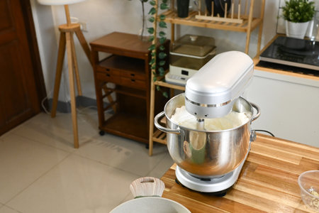 A silver food mixer sits on a wooden countertop in a kitchen.の写真素材