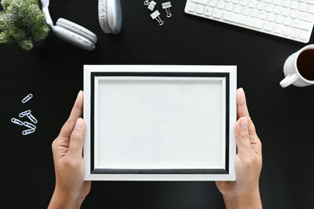 Hands holding blank picture frame top view office desk with work supplies and computer..の写真素材
