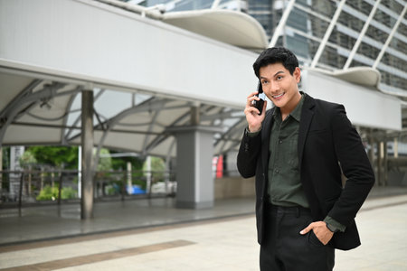 A man in a suit is talking on his cell phone while standing outside. He is in a good mood and is dressed professionally..の写真素材