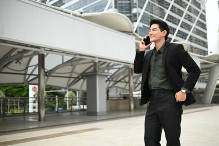A man in a suit is talking on his cell phone while standing outside. He is in a good mood and is dressed professionally.の写真素材