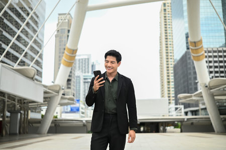 A man in a suit is talking on his cell phone while standing outside. He is in a good mood and is dressed professionally..の写真素材