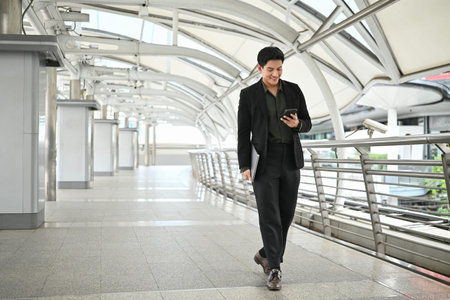 A man in a suit is walking with a cell phone in his hand and a folder in his other hand. Concept of professionalism and busyness.の写真素材