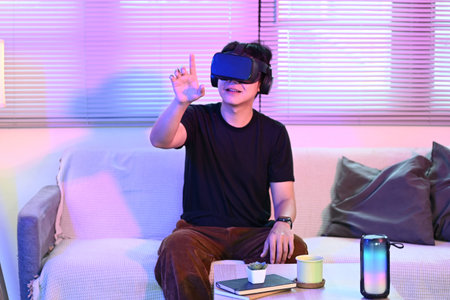 Man sitting on apartment living room couch wearing augmented reality glasses moving his hands while...