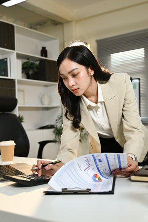A woman in a business suit is sitting at a desk with a stack of papers in front of herの写真素材