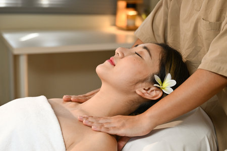A woman is lying on a massage bed and a masseuse is massaging her shoulders. The atmosphere is relaxing and peaceful..の写真素材