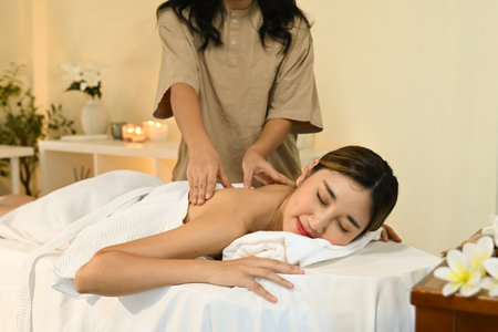 A woman is getting a massage from a massage therapist. She is smiling and relaxed. The massage table is covered with a white towel.の写真素材