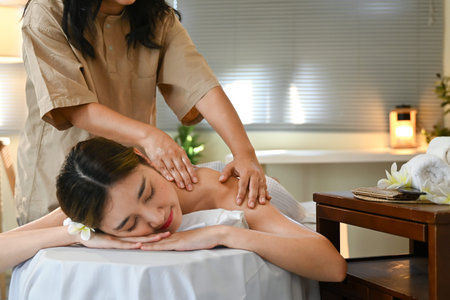 A woman is getting a massage from a massage therapist.The woman is smiling and she is enjoying the massage. The room is dimly lit, and there are candles on a table nearby.の写真素材