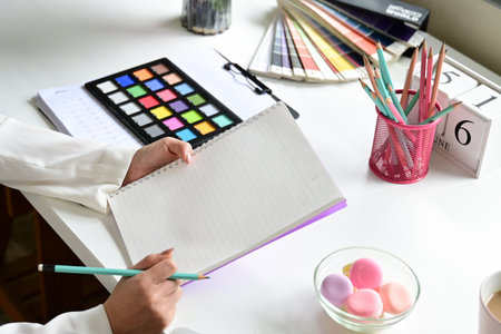 A woman writing in a notebook with a pencil. The notebook is on a table with a bowl of pastries and a cup of coffee. The person appears to be in a creative moodの写真素材