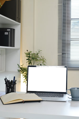A laptop sits on a desk with a notebook and a cup of coffee. The laptop is open to a blank screenの写真素材