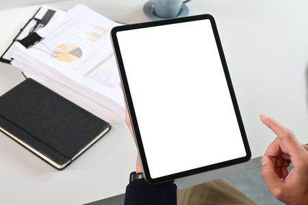 A person is holding a tablet with a white screen and a black book on the table. The tablet is pointing to a tabletの写真素材