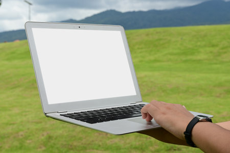 A person is holding a laptop in a grassy field. The laptop is open and the screen is blankの写真素材