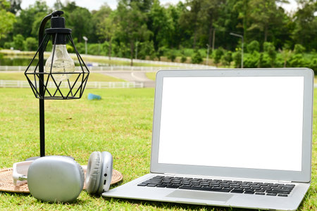 A laptop is open on a grassy field with a lamp and headphones nearby. The scene suggests a relaxed and leisurely atmosphere, possibly for someone to work or study outdoorsの写真素材