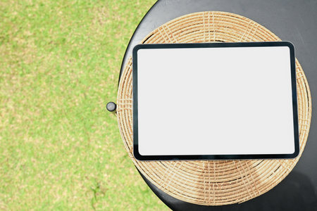 A tablet is sitting on a wicker plate on a table. The tablet is empty and the table is surrounded by grassの写真素材