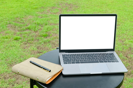 A laptop is open on a table next to a notebook with the green grassの写真素材