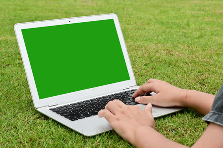 A person is typing on a laptop in a grassy field. The laptop screen is green, and the person is using a keyboard.の写真素材