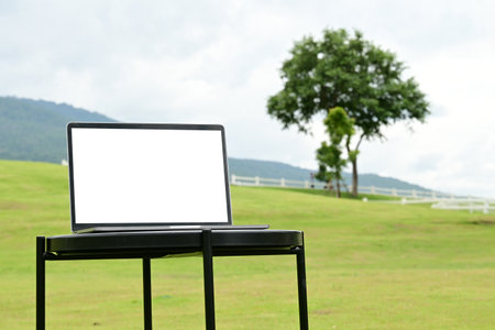 A laptop is open on a table in a grassy field. The grass is green and the sky is cloudy. The scene is peaceful and serene, with the laptop.の写真素材