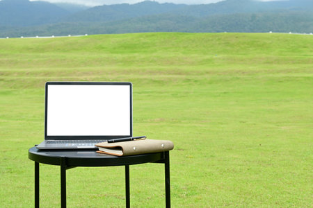 A laptop is open on a table in a grassy field. The grass is green and the sky is cloudy. The scene is peaceful and serene, with the laptopの写真素材