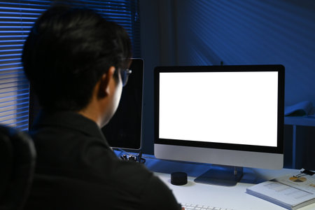 A man is sitting in front of a computer monitor with a black background. The monitor is blank.の写真素材