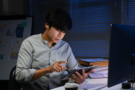 A man is sitting at a desk with a tablet in front of him. He is pointing at something on the screenの写真素材