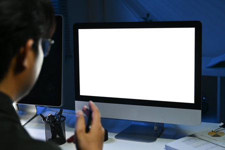A man is sitting in front of a computer monitor with a black background. The monitor is blankの写真素材