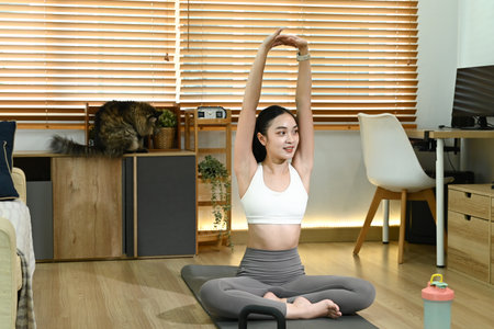 Smiling healthy Asian woman doing yoga shoulder stretching at home in living room.の写真素材