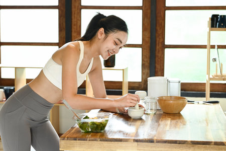 A woman is smiling while preparing food on a wooden table. She is wearing a white tank top and grey pantsの写真素材