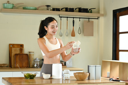 A woman is making a smoothie in a kitchen. She is smiling and she is enjoying herselfの写真素材
