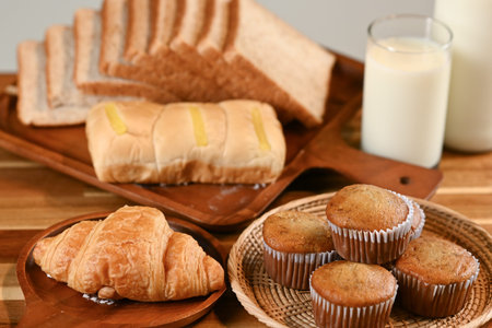 A loaf of freshly baked bread with slices, accompanied by a glass of milk on a wooden table,...