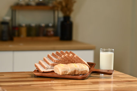 A tray of bread and a glass of milk sit on a wooden table. The bread is sliced and arranged on a...