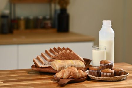 A loaf of freshly baked bread with slices, accompanied by a glass of milk on a wooden table, illuminated by warm sunlight in a cozy, rustic kitchen.の写真素材