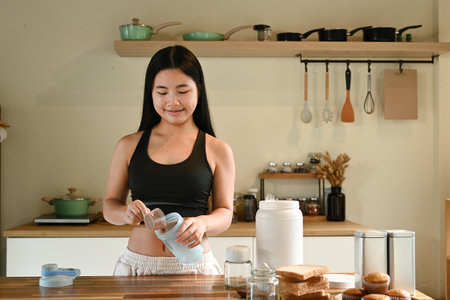 A woman is making a protein shakes in a kitchen. She is smiling and she is enjoying the processの写真素材