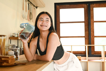 A woman is standing in a kitchen with a glass of protein shake in her hand.の写真素材
