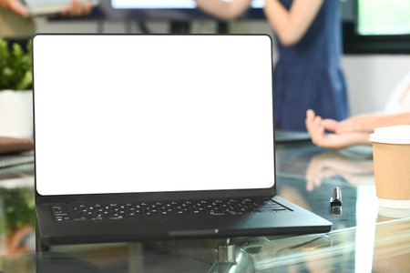 A laptop is open on a table with a person in the background. The laptop is black and the screen is blank.の写真素材