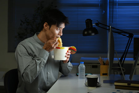 Asian young businessman eating noodles while working in office at night..の写真素材