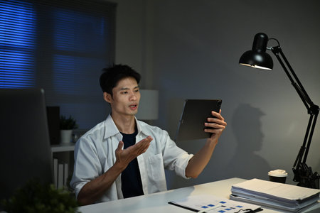 Asian businessman focus online video call meeting assignment on paperwork with colleague in tablet...