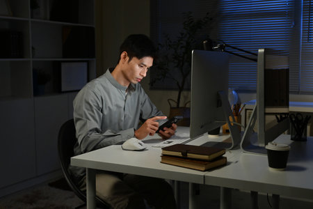 Staying late to get it done. Shot of a young businessman using a computer at his desk during a late night at work..の写真素材