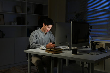 Shot of a young businessman using a laptop and smartphone during a late night in a modern office.の写真素材