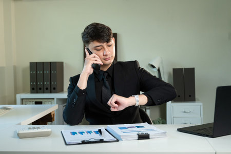 A man in a suit is talking on his cell phone while looking at the time on his wristwatchの写真素材