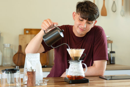 man brewing coffee with pour over method using a glass dripper in a kitchen.