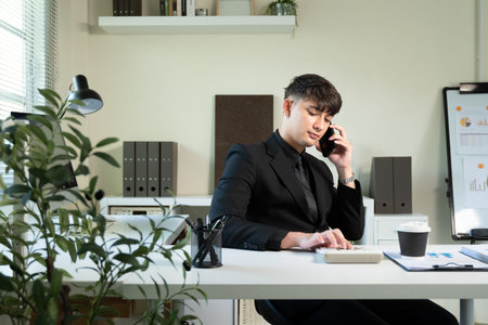A man in a suit is talking on his cell phone in office. The office is filled with office supplies...