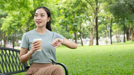 young Asian woman relaxing in a park, drinking a cup of coffee while surrounded by beautiful nature.の写真素材