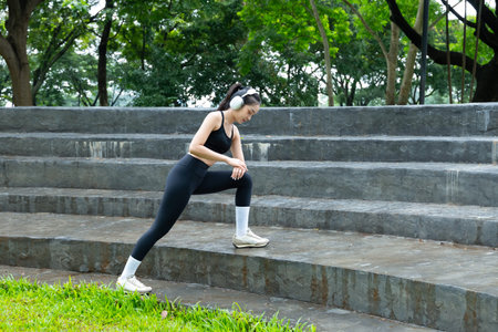 Young woman stretching legs and listening music with headphones in the park.