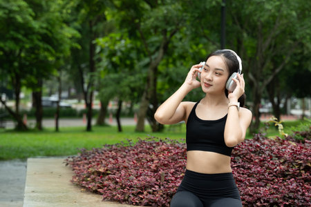 Young Asian Woman in Sports Outfit Wearing Headphones Outdoors in a Flowers Park, Enjoying Nature While Listening to Music.の写真素材