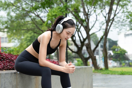 Young Asian Woman in Sports Outfit Wearing Headphones Outdoors in a Flowers Park, Enjoying Nature While Listening to Music.の写真素材