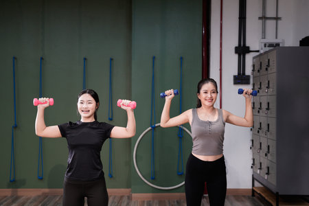 Two athletic women lifting dumbbells in a modern gym.