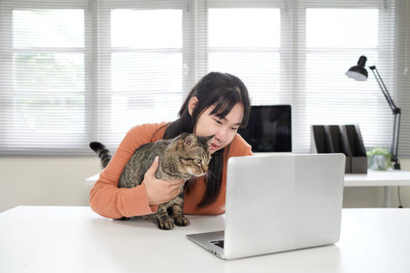 happy Asian business woman work from home office sitting at desk with cat using laptop.